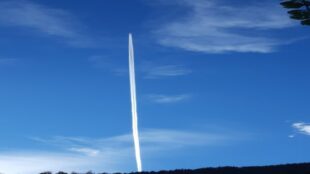 Flugzeug am Himmel, das einen Kondensstreifen hinter sich versprüht, der in Verschwörungstheorien als Chemtrail benannt wird