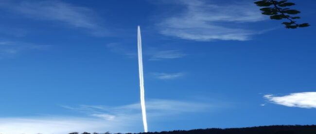 Flugzeug am Himmel, das einen Kondensstreifen hinter sich versprüht, der in Verschwörungstheorien als Chemtrail benannt wird